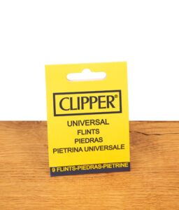 Gelbe Verpackung der Clipper Universal Feuersteine im 9er Pack stehend auf einer hellen Holzoberfläche.