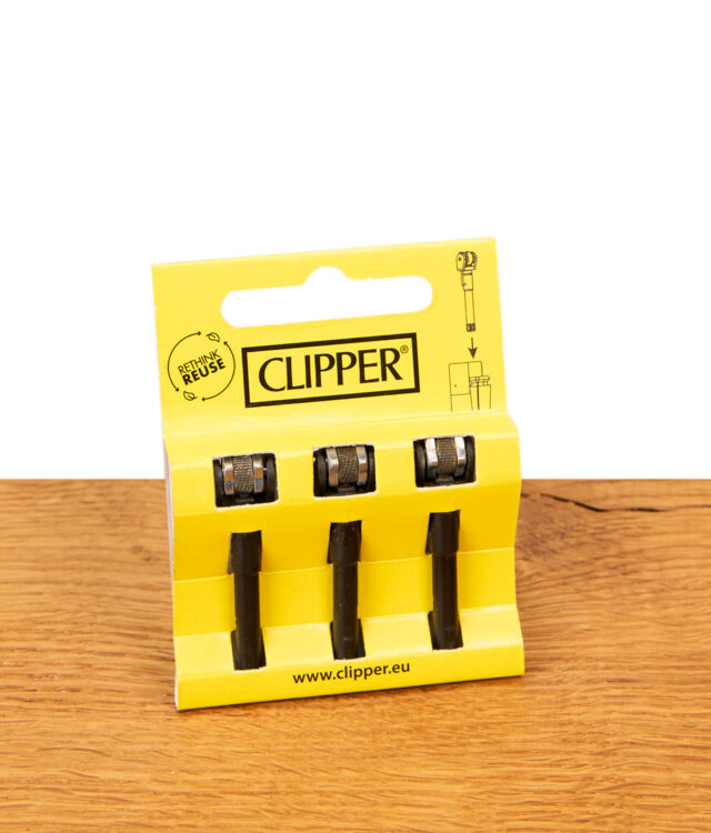 Gelbe Verpackung des Clipper Flintsystem 3er Pack. Schwarze Zündstifte mit Metallrädchen auf einem Holztisch.
