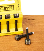 Clipper Flintsystem 3er Pack in gelbem Karton auf Holz. Davor liegen zwei entnommene Zündstifte mit Metallrädchen.