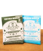 Grüne Nature of Spirit Kräutermischung Extra Weich neben der blauen Variante Wolken Weich. Zwei Sorten Tabakersatz auf Holz.