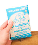 Hand hält die blaue Pouch-Tüte der Nature of Spirit Kräutermischung Wolken Weich. Nikotinfreier Tabakersatz über einem Holztisch.