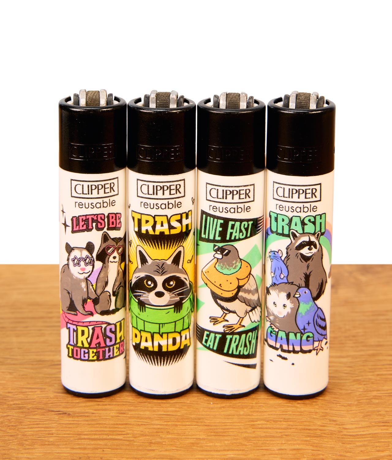 clipper-trash-gang-jpg Nachfüllbares Clipper Feuerzeug Trash Gang 4er-Set mit bunten Waschbär-Motiven stehend auf Holz.