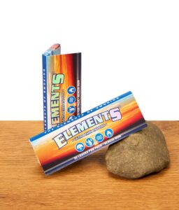 Zwei Elements 1 1/4 Size Papers Heftchen aus Reispapier dekorativ auf Holz und einem Stein arrangiert.