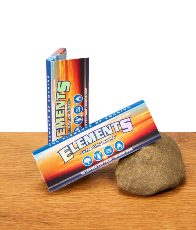 Zwei Elements 1 1/4 Size Papers Heftchen aus Reispapier dekorativ auf Holz und einem Stein arrangiert.