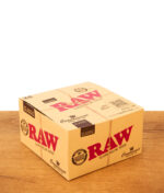 Geschlossene 24er-Displaybox der RAW Connoisseur King Size Slim Papers mit Tips auf Holztisch.